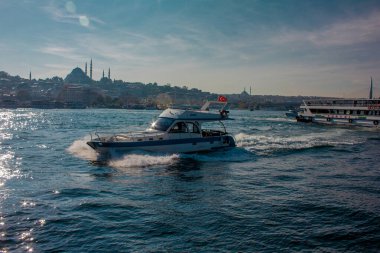 Eminonu, İstanbul, Türkiye-Ekim-Cumartesi-2021: Denizde küçük bir tekne hareket ediyor. Arkasında büyük bir yolcu feribotu var. Süleyman Camii ve Altın Boynuz Metro Köprüsü manzarası