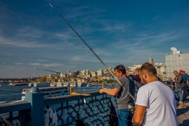 Eminonu, İstanbul, Türkiye-Ekim-Cumartesi-2021: Galata köprüsünde balık tutan insanlar. Bulutlu hava, Galata kulesi ve yolcu taşıyan feribot.