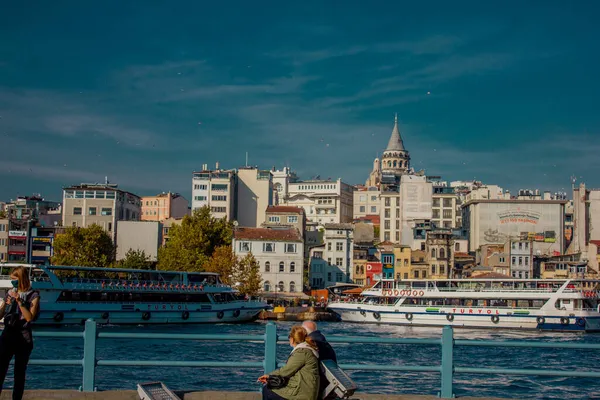 Eminonu, İstanbul, Türkiye-Ekim-Cumartesi-2021: Güneşin altında oturan iki yaşlı insan. Galata kulesi ve feribot manzarası