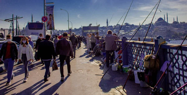 Eminonu, İstanbul, Türkiye-Ekim-Cumartesi-2021: Galata köprüsünde balık tutan insanlar. Bulutlu hava, Galata kulesi ve yolcu taşıyan feribot.
