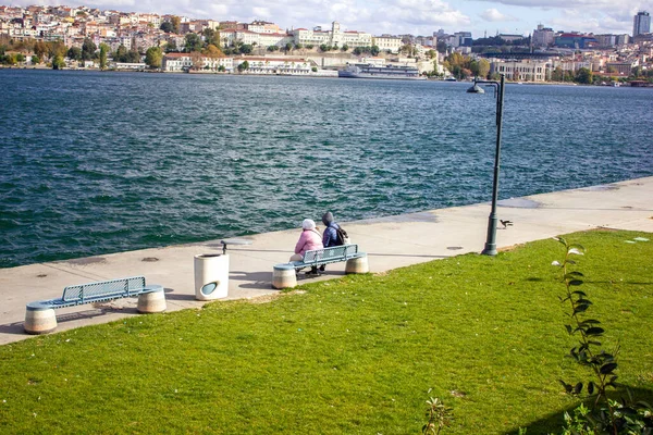Fatih, İstanbul, Türkiye-Ekim-Çarşamba-2021: Altın Boynuz 'un yanındaki bankta oturan iki şapkalı kadınlar