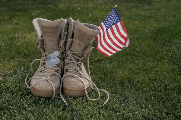 一个美国士兵的靴子 他作为英雄的象征回到家 带着一面美国国旗在风中飘扬 免版税图库图片