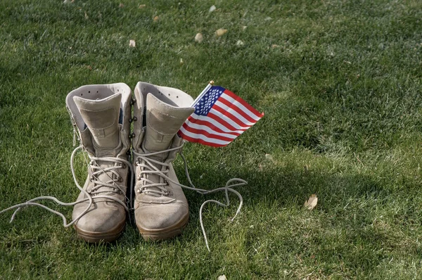 一个美国士兵的靴子 他作为英雄的象征回到家 带着一面美国国旗在风中飘扬 免版税图库照片