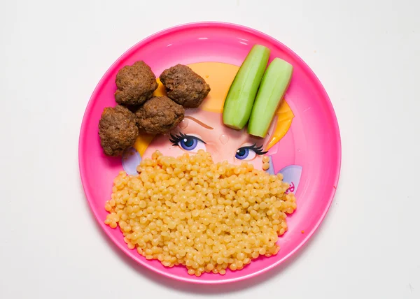Kinderen maaltijd roze plaat met vlees ballen komkommers en pasta — Stockfoto