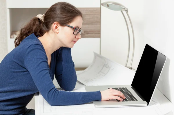 Giovane donna in occhiali seduta dietro il tavolo e guardando il computer portatile Foto Stock