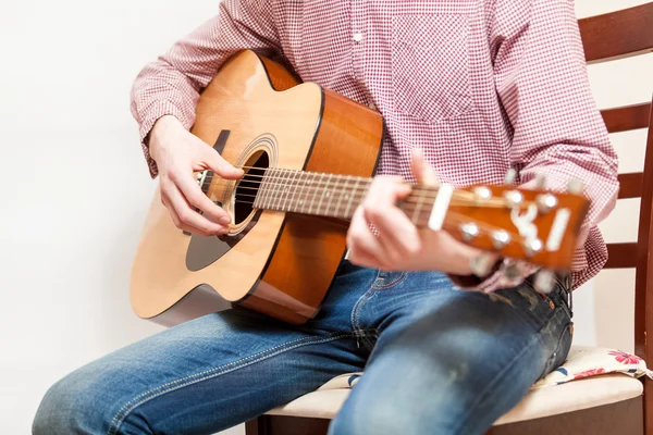 Foto di uomo seduto sulla sedia e che suona la chitarra acustica Immagini Stock Royalty Free