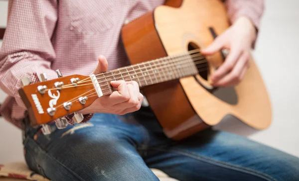 Mannen i jeans sitter och spelar gitarr Stockfoto
