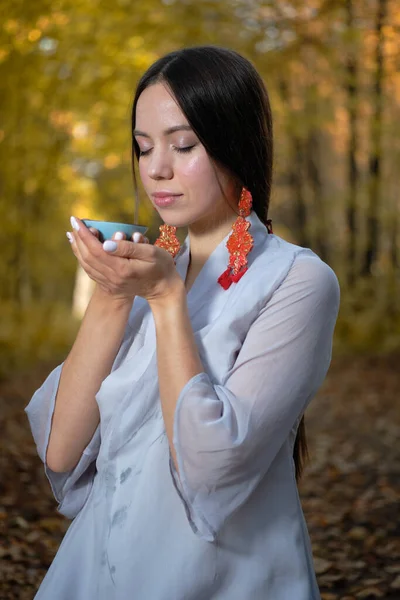 Dziewczyna w niebieskim kimono siedzi w jesiennym lesie i przygotowuje herbatę Zdjęcie Stockowe