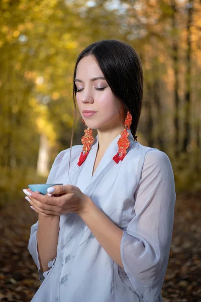 Une fille dans un kimono bleu se trouve dans la forêt d'automne et prépare le thé Photos De Stock Libres De Droits