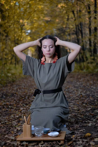 Młoda piękna dziewczyna siedzi na ziemi w nowoczesnych ubraniach w jesiennym żółtym lesie i gospodarstwa ceremonii herbaty Zdjęcia Stockowe bez tantiem