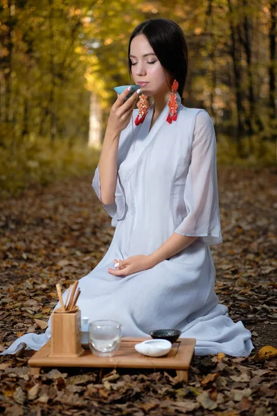 Dziewczyna w niebieskim kimono siedzi w jesiennym lesie i przygotowuje herbatę Obrazy Stockowe bez tantiem