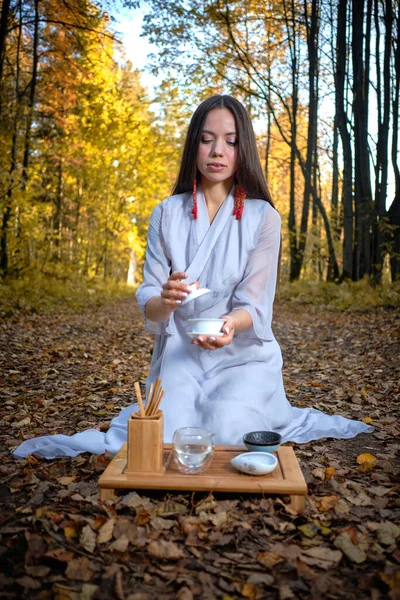 Dziewczyna w niebieskim kimono siedzi w jesiennym lesie i przygotowuje herbatę Obraz Stockowy