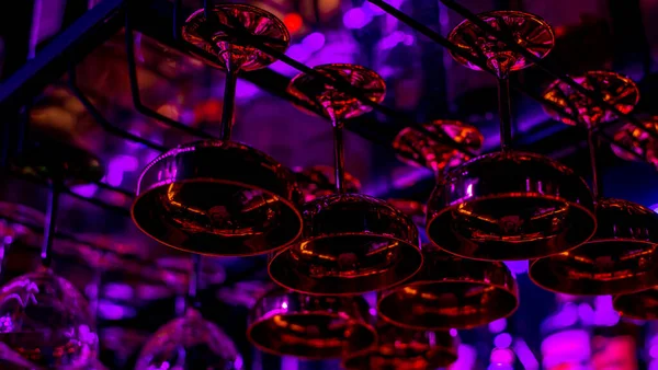 Glasses of cocktails. Glasses hanging above the bar in the restaurant. Empty glasses for wine. Cocktails martini glasses in shelf above a bar rack in restaurant. blue lights, blue background, night