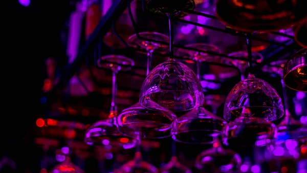 Glasses of cocktails. Glasses hanging above the bar in the restaurant. Empty glasses for wine. Cocktails martini glasses in shelf above a bar rack in restaurant. blue lights, blue background, night