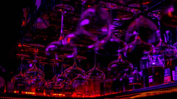 Glasses of cocktails. Glasses hanging above the bar in the restaurant. Empty glasses for wine. Cocktails martini glasses in shelf above a bar rack in restaurant. blue lights, blue background, night