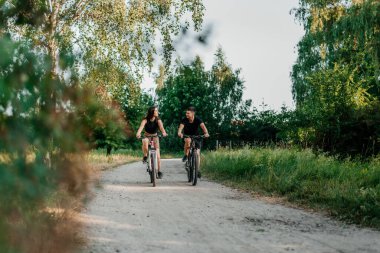 İnsanlar, eğlence ve yaşam tarzı konsepti - mutlu genç çift yazın yolda bisiklet sürüyor