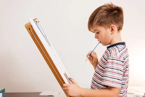 A boy paints a picture on an easel and paints