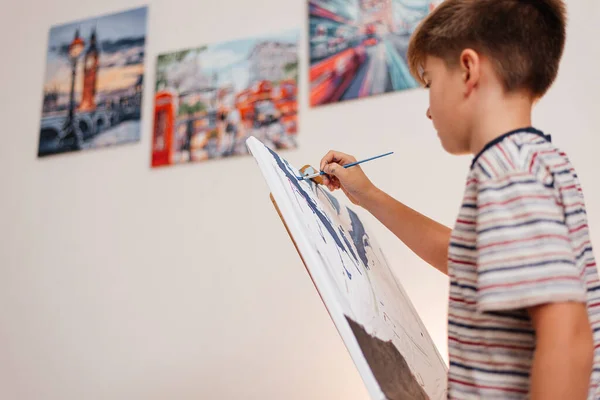 A boy paints picture with a brush on an easel