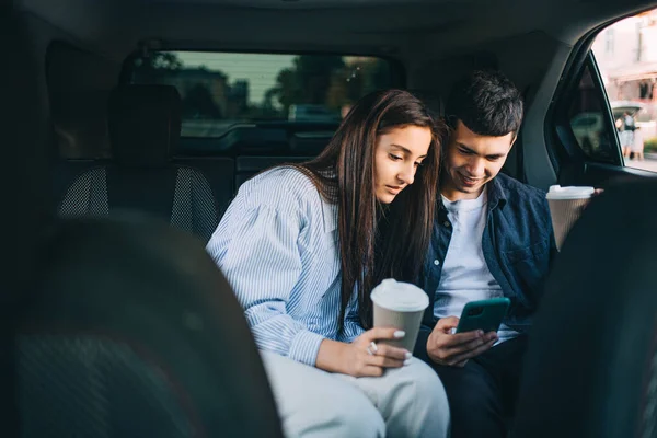 couple in the back seat of a taxi looks at their phone