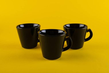 Üç siyah kupa, sarı arka plan. Kahve fincanları
