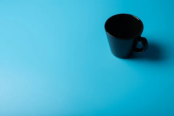 A black cup a blue background. Minimalism