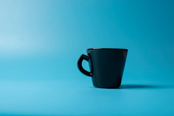 A black cup a blue background. Minimalism