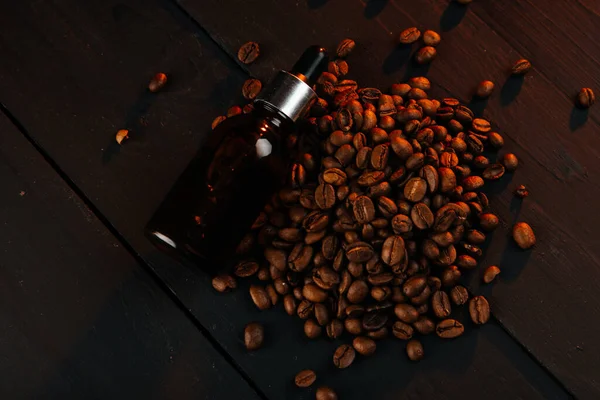 Essential oil with coffee beans on black wood background. Oils for beard.