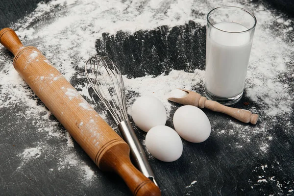 Ingredients for pastries: flour, eggs, milk against a dark background.
