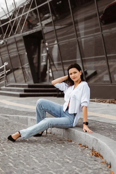A young woman poses outside in jeans and a white blouse