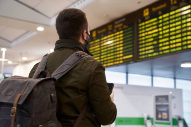 Havaalanında sırt çantalı genç bir adam uçuş çizelgesine bakıyor. seçici odak