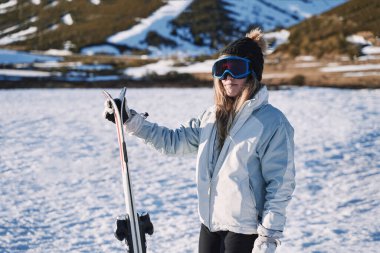 Şık, güzel kız dağda kayaklarıyla, gözlükleriyle ve şapkasıyla bekliyor..