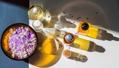 Sarı kozmetik şişeleri, beyaz masa manzarası üzerinde gerekli yağ zıt gölgeler. Spa, sağlık, rahatlama, vücut, yüz bakımı. Mor banyo tuzu. Güzellik ürünleri düz kopya alanı ile.