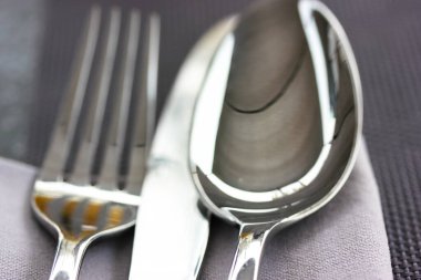 Metal çorba kaşığı, bıçak, çatal gri yüzey manzaralı gri bir peçetenin üzerinde yatıyor. Masa düzenleme, restoranda kumaş, kafe, ev mutfağı. Gri tekstil havlusu. Yukarıdaki çatal bıçak görüntüsünü kapat.