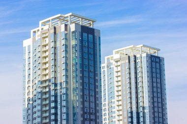 Güneşli bir günde mavi gökyüzüne karşı iki tane modern uzun apartman. Büyük şehirde simetrik modern mimarisi olan bina. Apartman dairesi. Emlak yatırımları, satın alma, kiralama. İş merkezi