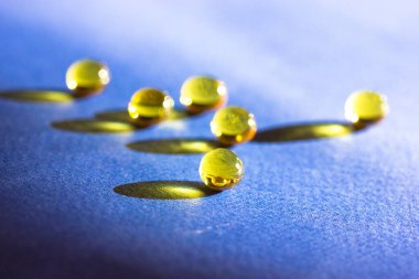 Sarı renkli balık yağı hapları, tabletler, omega 3 jelatin kapsülleri mavi masada uzanıyor ve karşıt uzun gölgeler oluşuyor. Tıbbi, sağlık, ilaç tedavisi asgari arkaplan görüşü.