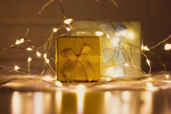 黄色礼品盒上的蝴蝶结站在桌子上 中间闪烁着五彩缤纷的花环灯 2022年新年 圣诞节 神奇的寒假购物 金色盒子 晚上有礼物 节日背景 — 图库照片