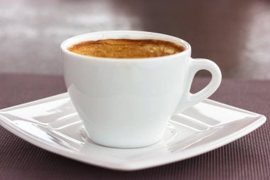 Yuvarlak beyaz seramik bardak, kapuçino, kahve köpüğü ve kahve tabağı. Bir kafede sıcak aromalı bir içecek, sabahları restoran, sonbahar mevsiminde öğle yemeği. İçecek teması.