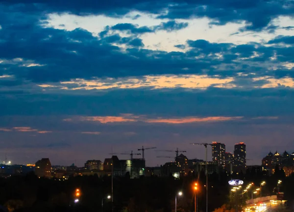 Панорама большого города ночью с видом на высотные здания на горизонте. Сумерки в городе. Размытое городское прошлое. Огни в окнах, уличные фонари против темно-синего облачного неба — стоковое фото