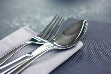 Çorba kaşığı ve metal çatal gri yüzey manzaralı gri bir peçetenin üzerinde yatar. Masa düzenleme, restoranda kumaş, kafe, ev mutfağı. Gri tekstil havlusu. Yukarıdaki çatal bıçak görüntüsünü kapat.