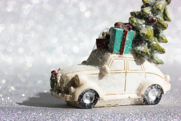White toy truck car with green Christmas tree on roof rides on a silvered shining background. Minimalistic happy New Years Eve background. Greeting card, copy space. Christmas gift boxes delivery. — Fotografia de Stock