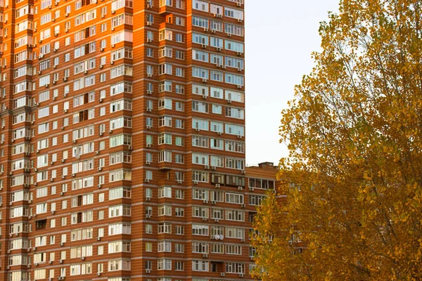 Kijów, Ukraina. 8 października 2021. Czerwona cegła wielopiętrowy nowoczesny dom wznosi się przeciwko jesiennemu niebu. Drzewo z żółtymi liśćmi w tle ogromnego wysokiego budynku mieszkalnego. Jesienny sezon jesienny w wielkim mieście — Zdjęcie stockowe