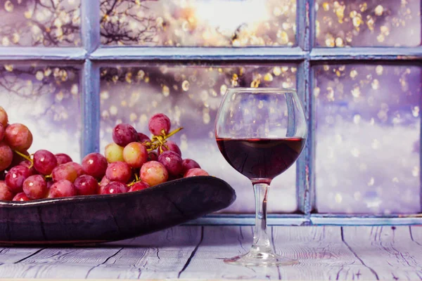 Uvas, copo de vinho tinto em uma mesa contra janela. Alcoólico de frutos de Natureza morta. — Fotografia de Stock