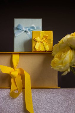 Sarı ve mavi hediye kutuları koyu gri arka planda, sarı Austin gül buketi. Hediyeli tebrik kartı, doğum günü hediyeleri, Anneler Günü, yıldönümü, 2022. Alışveriş, satış, hediye..