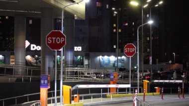 Kyiv, Ukrayna, 1 Ekim 2021. Otoparktan çık. Otomatik bariyer sistemi. Otopark bariyeri yükseliyor ve kırmızı araba gece bir şehir caddesine gidiyor. Metin durdurmalı kırmızı yol işaretleri.