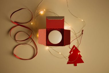 İçinde beyaz kavanoz olan açık bir hediye kutusu, yanan çelenk, süs, kırmızı Noel ağacı ışıklarının arasında bir masanın üzerinde duruyor. Yeni yıl sürprizi, mevcut 2022. Noel arifesi. Yüz bakımı kozmetik ürünleri.