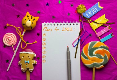 2022 için metin planlı defter. Tatlı tatlılar, zencefilli çörek adam, lolipop kaplan şeklinde çörekler, Yeni Yıl sembolü. Noel 'i pembe ile kutlamak için Tinsel dekor, çok renkli yıldızlar.