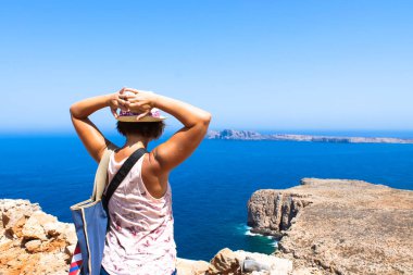 Gramvousa Adası, Yunanistan. Temmuz 2017. Hasır şapkalı bir turist, elleri dağın kenarında dikilirken uzaklara bakar. Balos Gölü 'nün sakin mavi sularıyla Akdeniz.