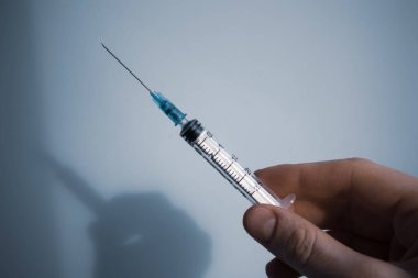 2,5 ml şırınga. Kadının elinde steril. Mavi arka planda. Salgın sırasında sağlık, ilaç, aşı, koronavirüs, grip, diğer hastalıklar konsepti. 
