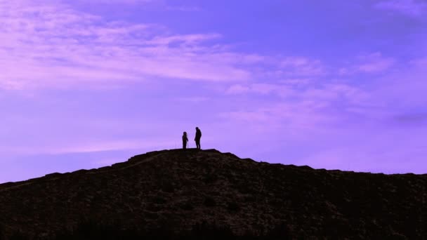 父と息子の丘の上に青い紫色の曇りの空に対して立っている 子供の頂上を征服している 達成コンセプト 親と子供の山の上に ピーク時の人々のシルエット — ストック動画