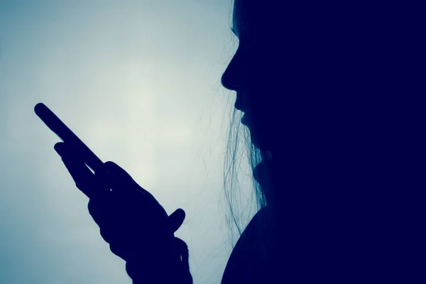 스마트폰을 배경을 스크롤하는 소녀의 실루엣 휴대폰을 사용하여 프로필에 나타난 인터넷에서 — 스톡 사진